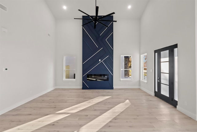 unfurnished living room featuring a high ceiling, light hardwood / wood-style flooring, and ceiling fan