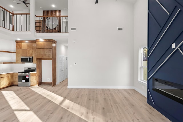 kitchen featuring a high ceiling, light wood-type flooring, stainless steel appliances, and ceiling fan