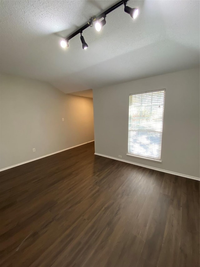 unfurnished room featuring rail lighting, a textured ceiling, and dark hardwood / wood-style flooring