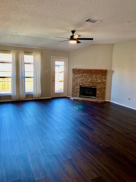 unfurnished living room with ceiling fan, dark hardwood / wood-style floors, a brick fireplace, and a textured ceiling