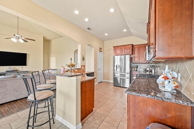 kitchen with appliances with stainless steel finishes, backsplash, a breakfast bar, dark stone countertops, and lofted ceiling