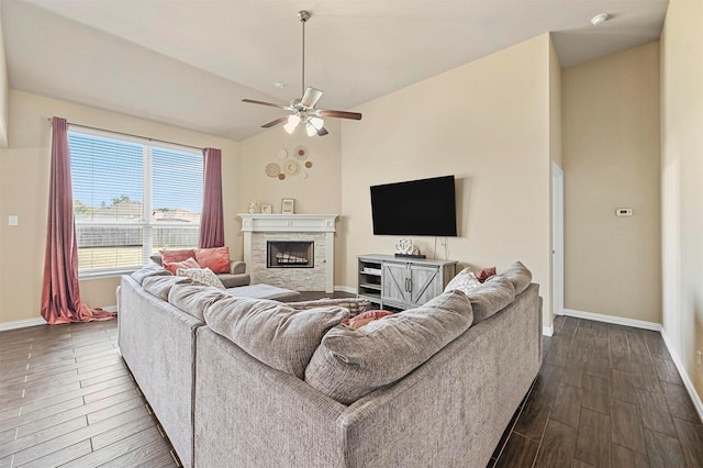 living room featuring hardwood / wood-style flooring, ceiling fan, a stone fireplace, and lofted ceiling