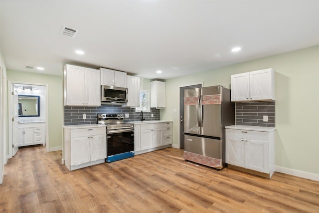 kitchen with white cabinets, appliances with stainless steel finishes, backsplash, and light hardwood / wood-style floors