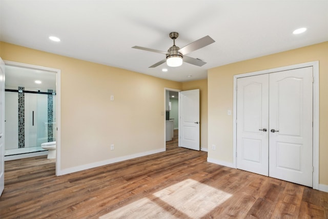 unfurnished bedroom featuring hardwood / wood-style flooring, ceiling fan, a barn door, connected bathroom, and a closet