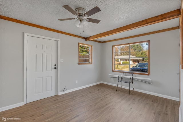 empty room featuring ceiling fan, beamed ceiling, light hardwood / wood-style floors, and a textured ceiling