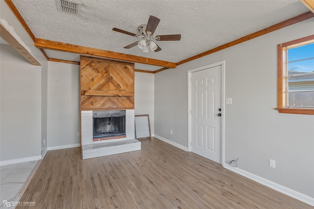 unfurnished living room featuring beamed ceiling, light wood-type flooring, ceiling fan, a brick fireplace, and a textured ceiling