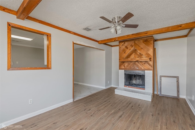 unfurnished living room featuring light hardwood / wood-style flooring, ceiling fan, a fireplace, a textured ceiling, and beamed ceiling