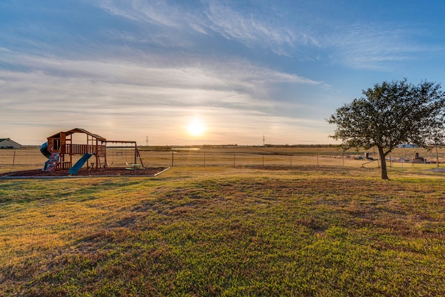 yard at dusk featuring a rural view, a playground, and fence