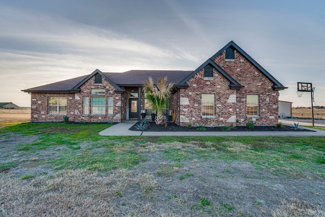 view of front facade featuring brick siding, roof with shingles, and a front yard