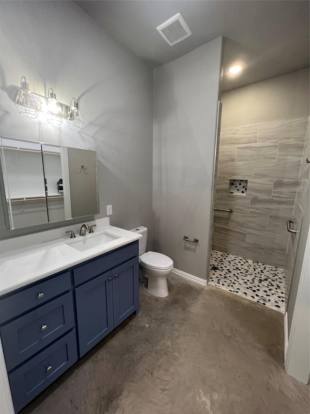 bathroom featuring toilet, vanity, concrete floors, and tiled shower