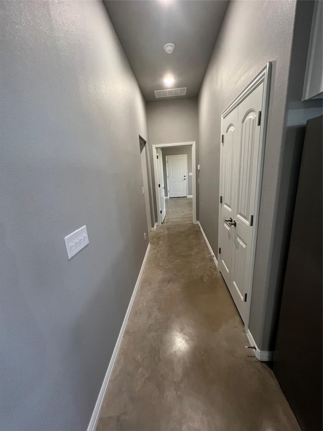 corridor with visible vents, concrete floors, and baseboards