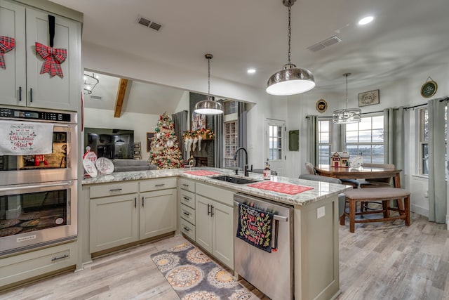 kitchen featuring sink, stainless steel appliances, kitchen peninsula, decorative light fixtures, and light wood-type flooring