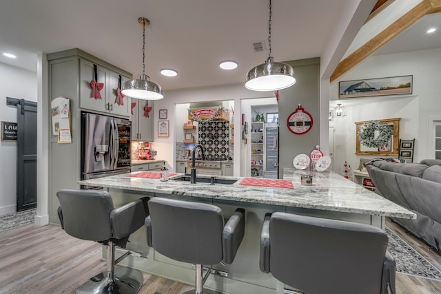 kitchen featuring light stone countertops, sink, pendant lighting, light hardwood / wood-style flooring, and stainless steel fridge with ice dispenser