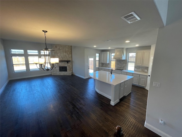 kitchen with premium range hood, white cabinetry, decorative light fixtures, an island with sink, and a fireplace