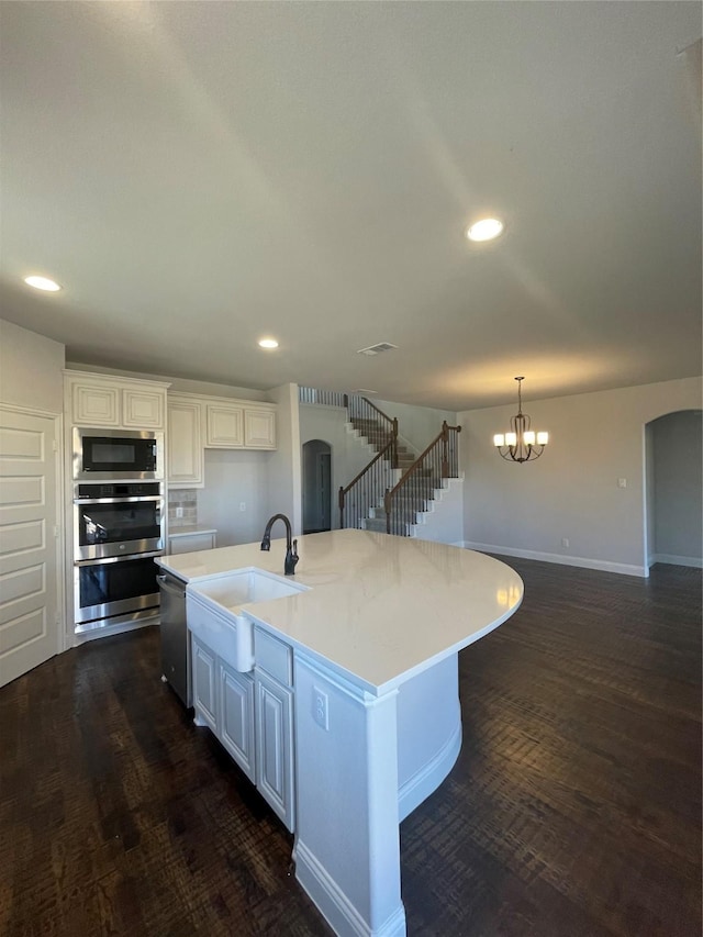 kitchen with sink, hanging light fixtures, stainless steel appliances, a kitchen island with sink, and white cabinets