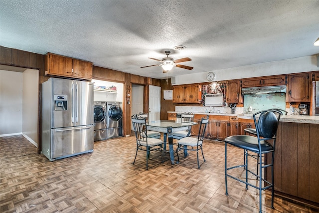 kitchen featuring ceiling fan, washing machine and dryer, a textured ceiling, stainless steel fridge with ice dispenser, and light parquet flooring