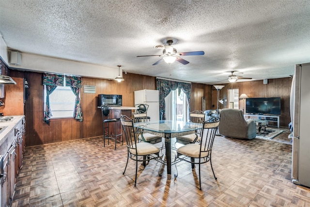 dining area with ceiling fan, wood walls, a textured ceiling, and light parquet floors