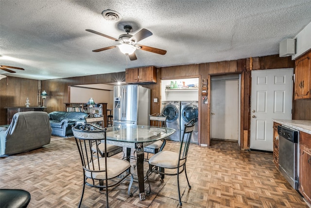 dining area featuring independent washer and dryer, a textured ceiling, light parquet floors, and wood walls