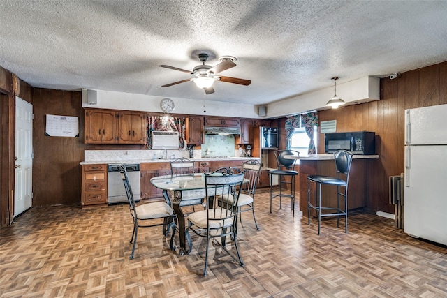 kitchen with stainless steel dishwasher, a textured ceiling, light parquet floors, white refrigerator, and wood walls