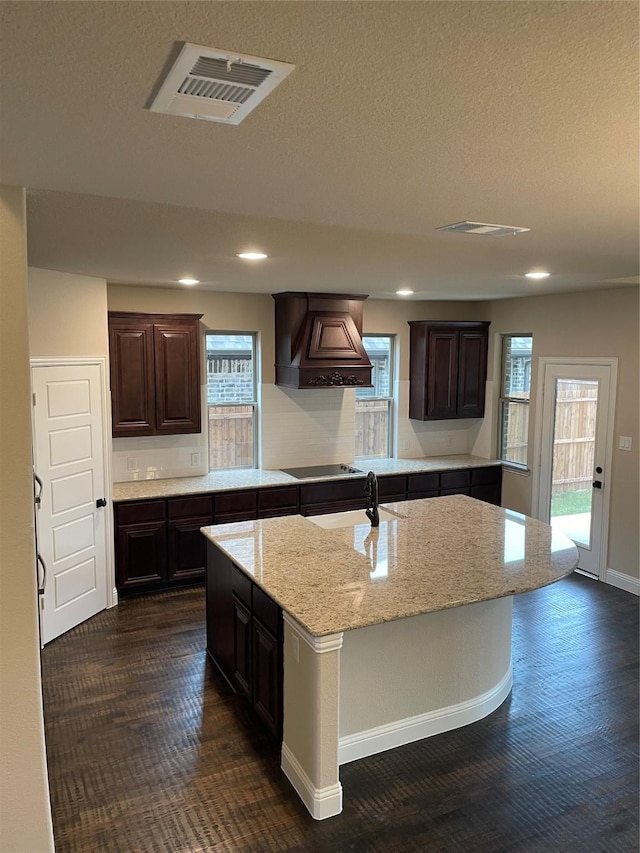 kitchen featuring sink, dark brown cabinets, a center island with sink, and premium range hood