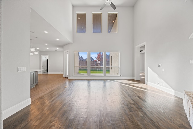 unfurnished living room featuring dark hardwood / wood-style flooring, a towering ceiling, and ceiling fan