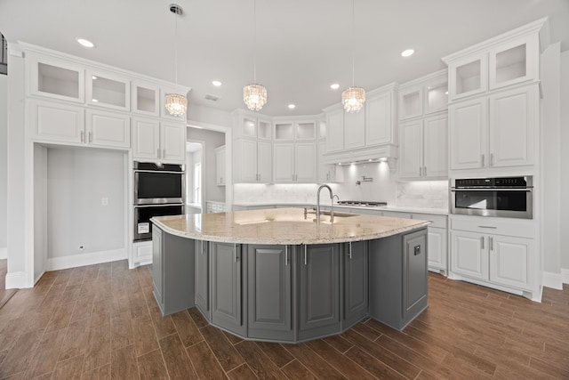 kitchen featuring light stone counters, decorative light fixtures, a kitchen island with sink, and white cabinets