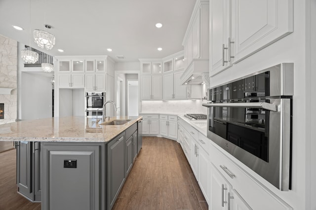 kitchen with gray cabinets, an island with sink, sink, white cabinets, and light stone counters