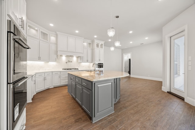 kitchen with hanging light fixtures, a center island with sink, gray cabinets, stainless steel appliances, and white cabinets