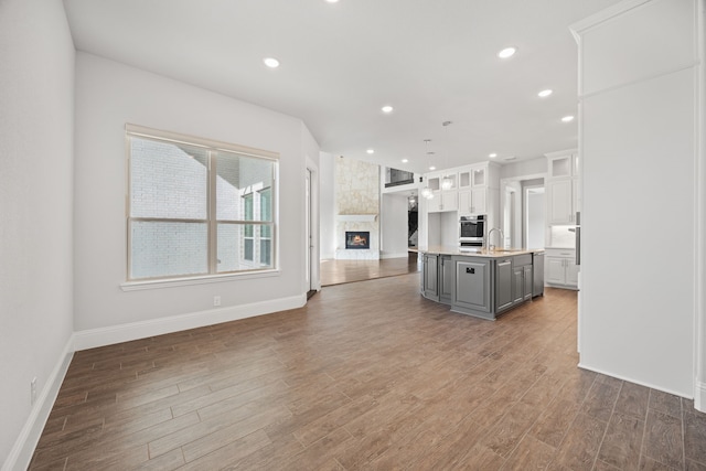 kitchen featuring gray cabinetry, white cabinetry, stainless steel oven, decorative light fixtures, and a center island with sink