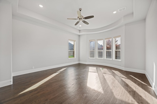 empty room featuring ceiling fan, a tray ceiling, and dark hardwood / wood-style flooring