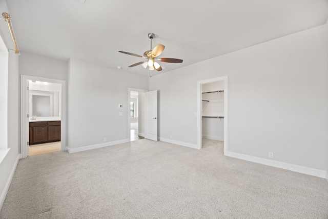 unfurnished bedroom with ensuite bathroom, a spacious closet, light carpet, a closet, and ceiling fan