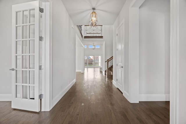 corridor featuring a high ceiling, a notable chandelier, and dark hardwood / wood-style flooring