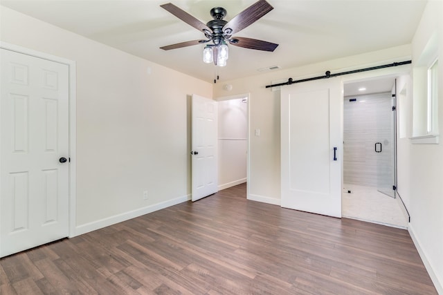 unfurnished bedroom featuring a barn door, ceiling fan, and dark wood-type flooring