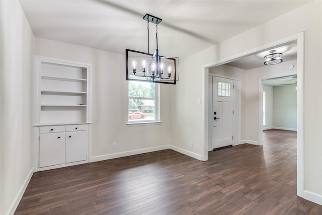 unfurnished dining area featuring dark hardwood / wood-style flooring, built in features, and an inviting chandelier