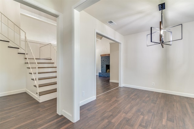 interior space featuring a brick fireplace, dark wood-type flooring, and a notable chandelier