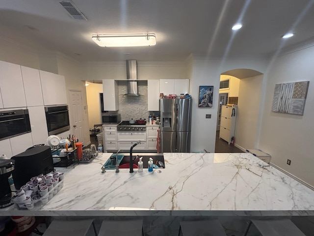 kitchen with appliances with stainless steel finishes, white cabinetry, sink, decorative backsplash, and wall chimney range hood