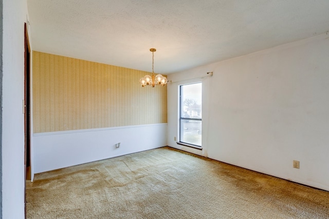 empty room with carpet flooring, a textured ceiling, and a notable chandelier