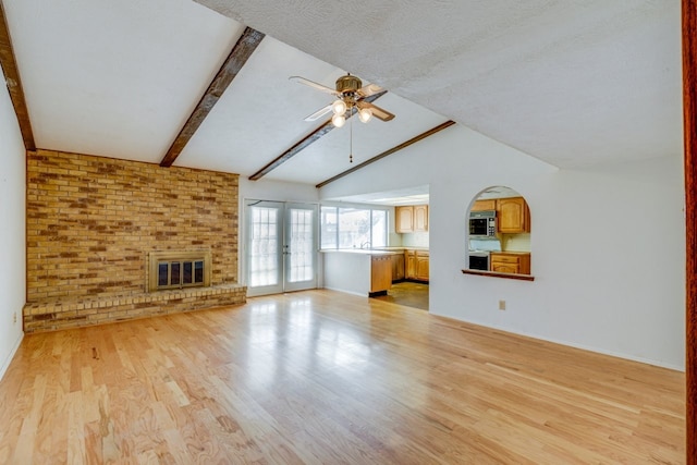 unfurnished living room with ceiling fan, french doors, vaulted ceiling with beams, light hardwood / wood-style flooring, and a fireplace