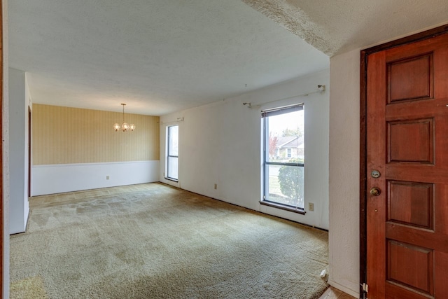 carpeted spare room featuring a textured ceiling and an inviting chandelier