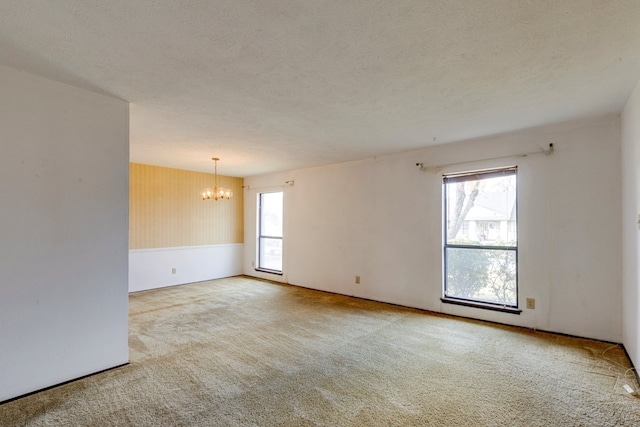 empty room with light carpet, a textured ceiling, and an inviting chandelier