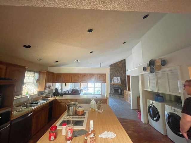 kitchen with stainless steel appliances, vaulted ceiling, sink, separate washer and dryer, and a fireplace