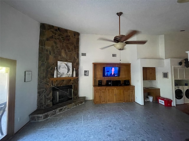 living room with a towering ceiling, a textured ceiling, ceiling fan, washing machine and clothes dryer, and a stone fireplace