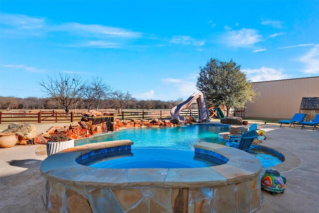 view of pool with a rural view, a patio area, an in ground hot tub, and a water slide