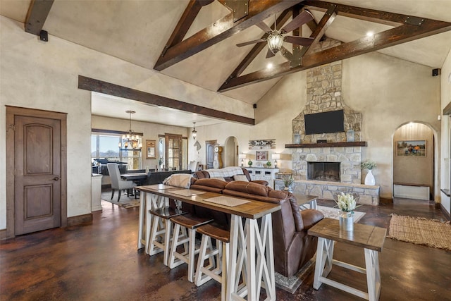 living room with beamed ceiling, a stone fireplace, ceiling fan with notable chandelier, and high vaulted ceiling