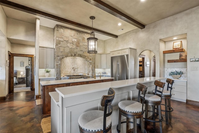 kitchen with appliances with stainless steel finishes, pendant lighting, a kitchen bar, beam ceiling, and a spacious island