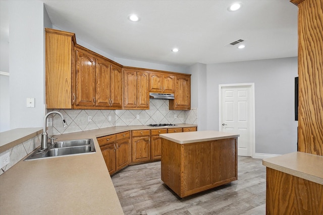 kitchen with a kitchen island, sink, light wood-type flooring, and decorative backsplash