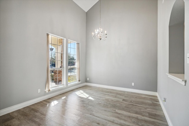 spare room with a towering ceiling, hardwood / wood-style floors, and an inviting chandelier