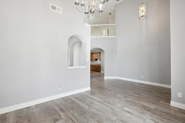 unfurnished dining area with hardwood / wood-style flooring, a towering ceiling, and a notable chandelier