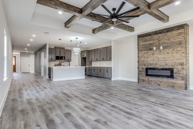 unfurnished living room featuring beam ceiling, light hardwood / wood-style flooring, ceiling fan, and a stone fireplace