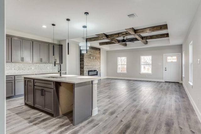 kitchen featuring light wood-type flooring, backsplash, ceiling fan, beam ceiling, and an island with sink